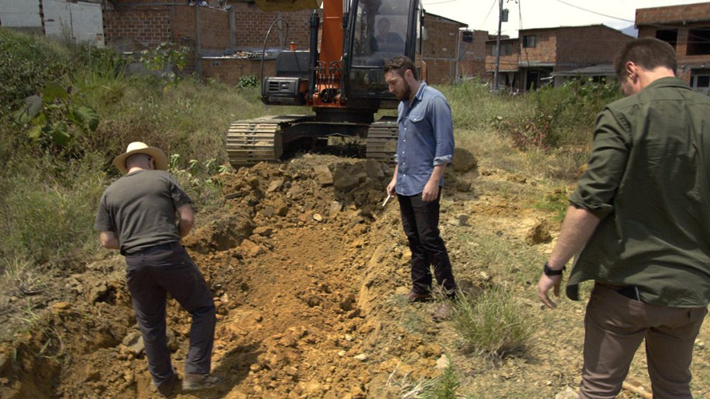 Doug Laux and Paul Bauman examine the unearthed dirt of an empty field in Barrio Pablo Escobar, hoping to find buried cash.