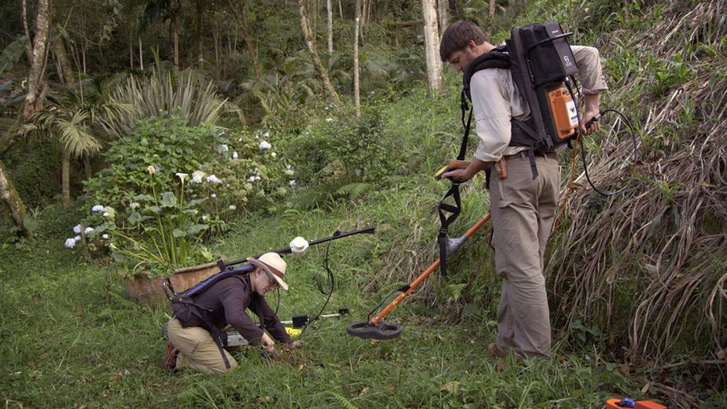Ground-penetrating-radar team Paul Bauman and Colin Miazga run a metal detector over some jungle ground.