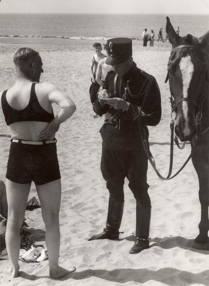 Strandtafereel. Marechaussee bekeurt een badgast die onvoldoende gekleed is op het strand. Nederland, Heemskerk, 1931.